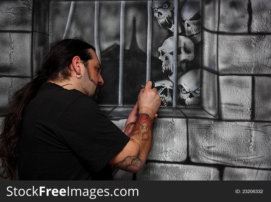 A man with tattoos make drawing on a wall painting skulls behind bar. A man with tattoos make drawing on a wall painting skulls behind bar