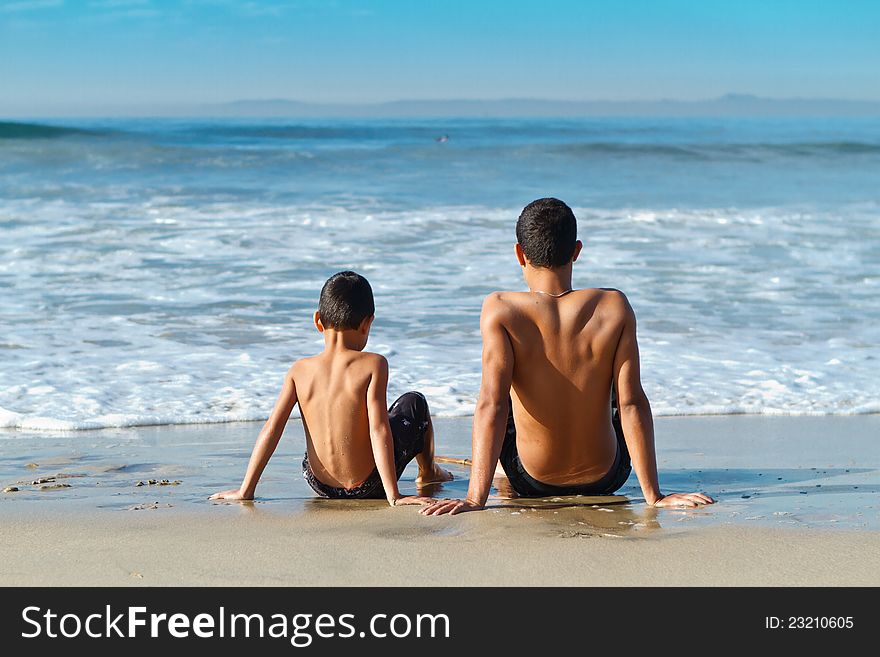 Two brothers relaxing at the water's edge after a fun day of playing at Huntington Beach. Two brothers relaxing at the water's edge after a fun day of playing at Huntington Beach.