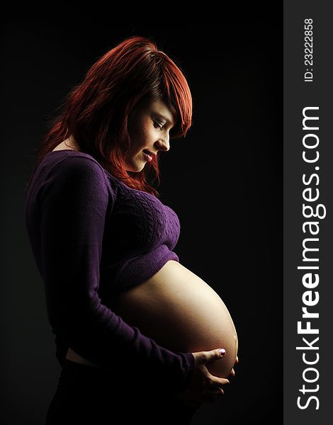 Young woman pregnant holding her tummy against a dark background. Young woman pregnant holding her tummy against a dark background