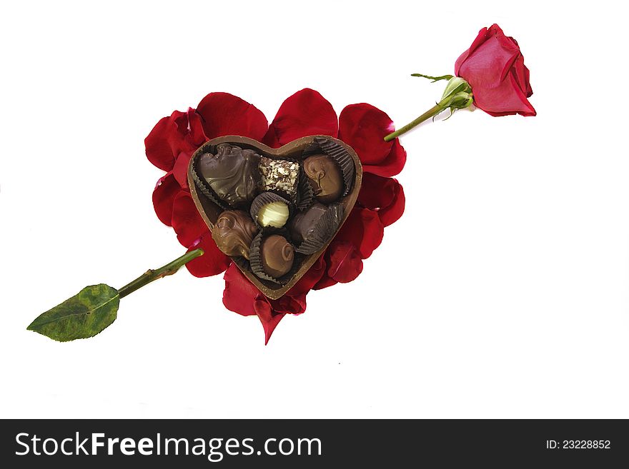 Photo of Fancy chocolates in a chocolate heart shaped container arranged on a heart-shaped bed of red rose petals with a piercing rose arrow. Photo of Fancy chocolates in a chocolate heart shaped container arranged on a heart-shaped bed of red rose petals with a piercing rose arrow