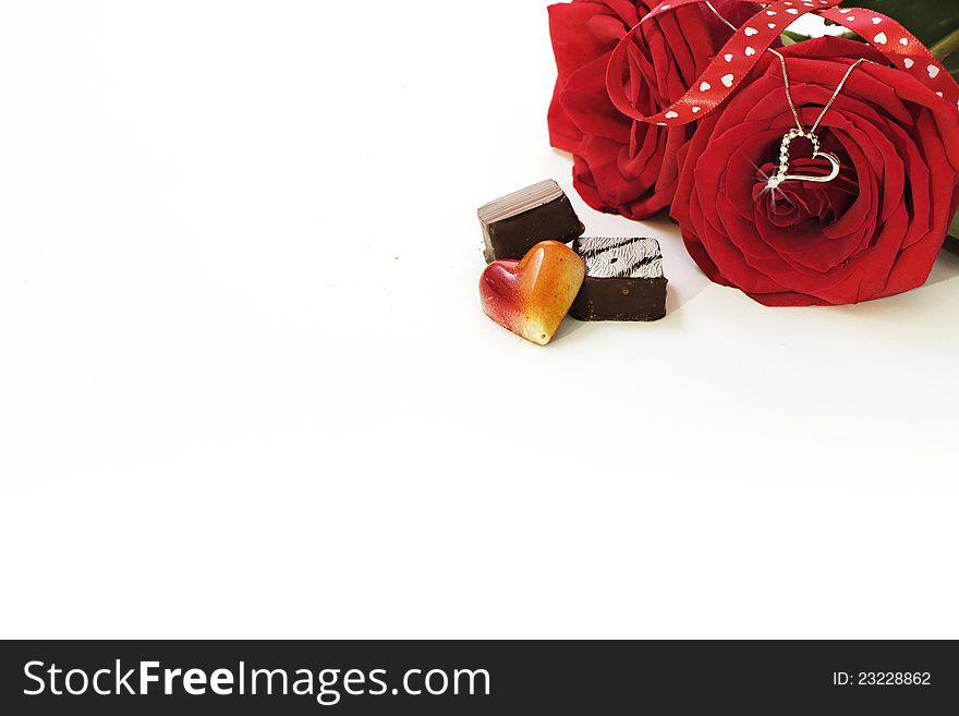 A still life composition of a White Gold and Diamond necklace hanging from a red rose with fancy chocolates on the foreground and lots of copy space. A still life composition of a White Gold and Diamond necklace hanging from a red rose with fancy chocolates on the foreground and lots of copy space.