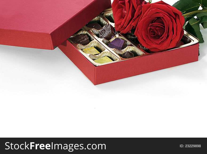 A Still life composition of a gold diamond engagement ring with a red box of fancy chocolates and red roses. A Still life composition of a gold diamond engagement ring with a red box of fancy chocolates and red roses