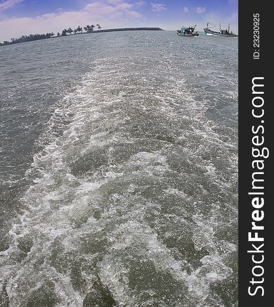 Wake or trail from a boat in arabian sea with fishing boats and shore visible in the backdrop. Photo taken near Udupi, Karnataka, India