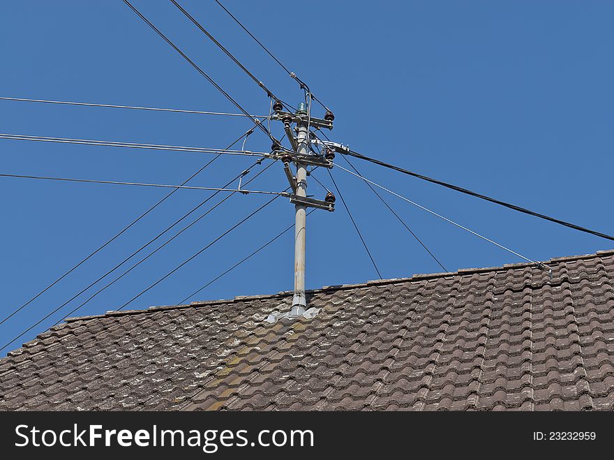 Electric transmission wires connected to a post on top of a house in Germany with a traditional tile roof