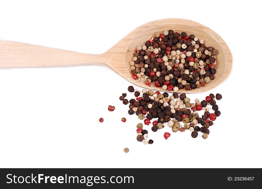 Lots of ground pepper of different colors on light brown wooden spoon over white background