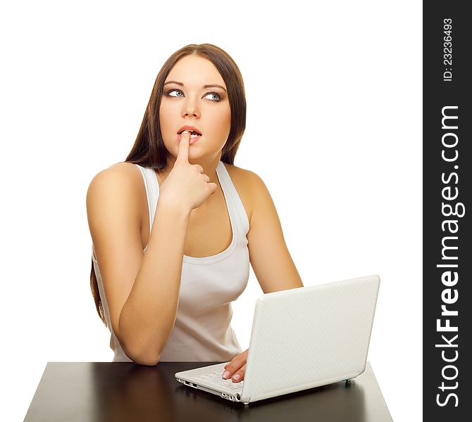 The young woman thinks with the laptop behind a table on a white background. The young woman thinks with the laptop behind a table on a white background