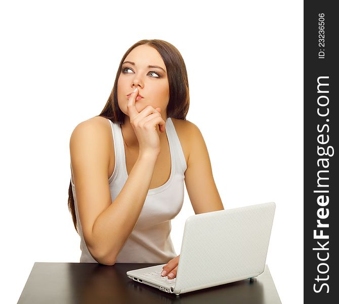 The young woman thinks with the laptop behind a table on a white background. The young woman thinks with the laptop behind a table on a white background