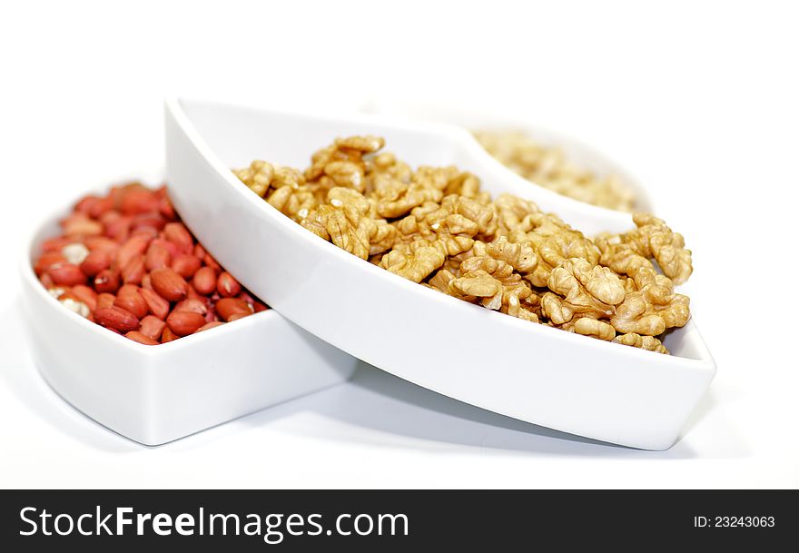 White plats with walnuts, peanut and pine nut on white background