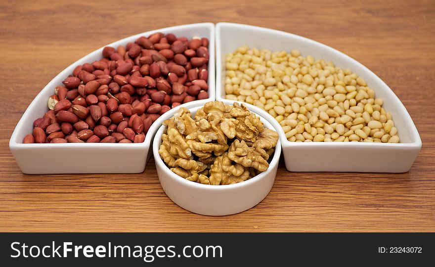 White plats with walnuts, peanut and pine nut  on wooden background