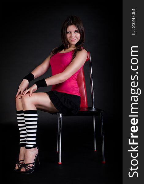 Young model sits on a red chair. Black  background.