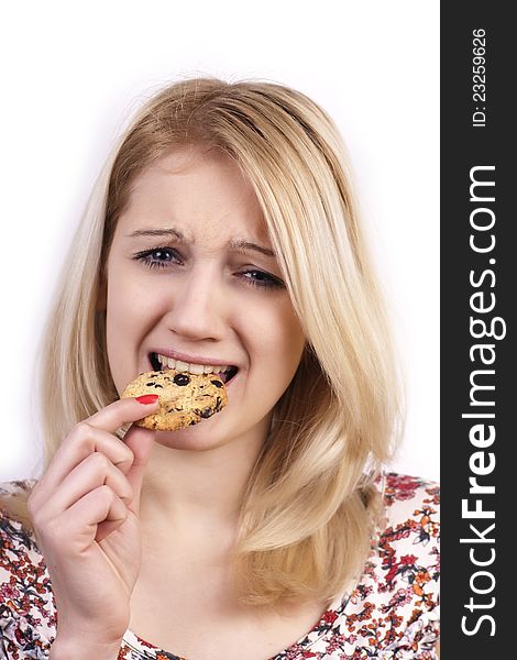 Young woman eating cookie with grimace on white background