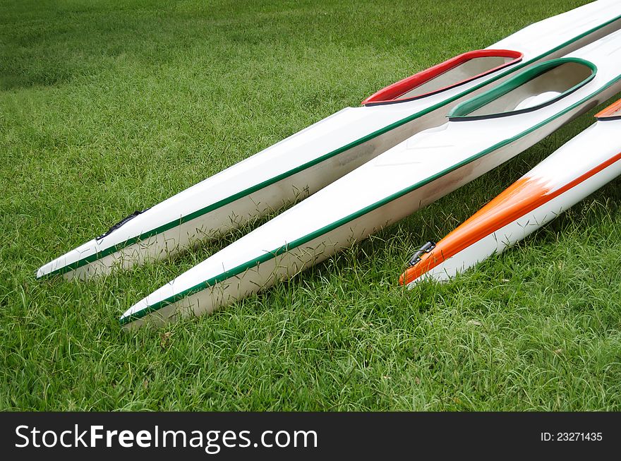 Three colourful K1 sprint kayaks with long pointy beams lying on green grass. Three colourful K1 sprint kayaks with long pointy beams lying on green grass