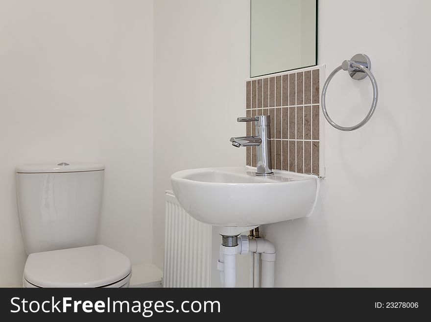 Basic cloakroom suite of white porcelain WC and basin with tiled splashback