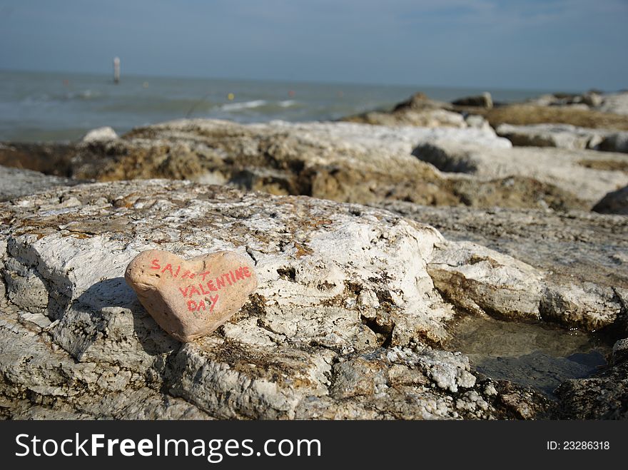 Declaration of happy saint valentine's day of a couple's lovers on a stone heart over some rocks next to the Adriatic sea. Declaration of happy saint valentine's day of a couple's lovers on a stone heart over some rocks next to the Adriatic sea