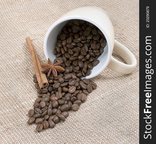 Coffee is a bob, the sticks of cinnamon and anise pour out from a mug on a background sacking