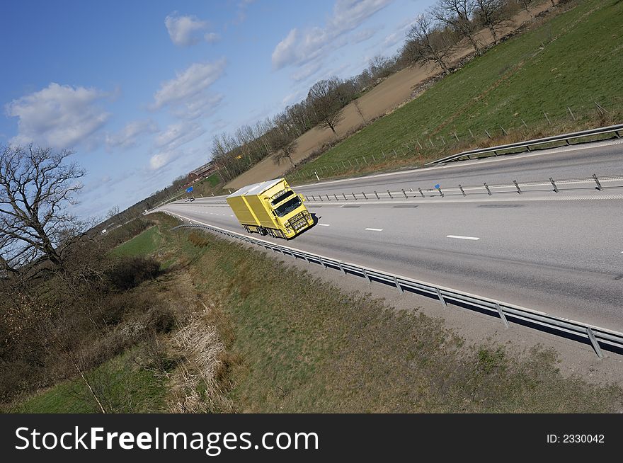 Distant clean yellow truck on highway surrounded by country-side. Distant clean yellow truck on highway surrounded by country-side