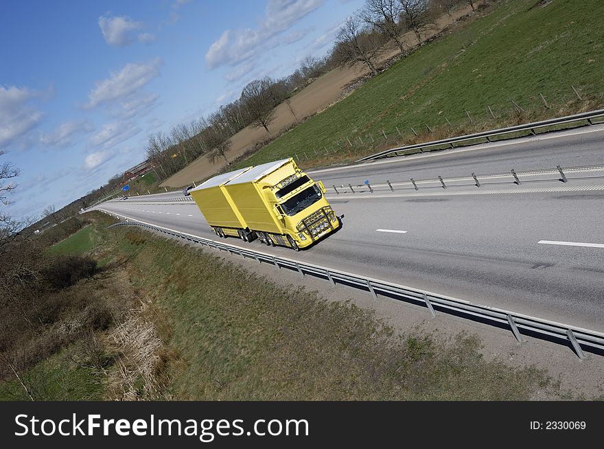 Large yellow truck speeding on long highway-straight. country-side in background. Large yellow truck speeding on long highway-straight. country-side in background