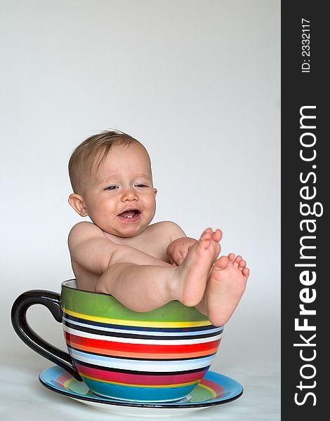 Image of an adorable baby sitting in a colorful, over-sized teacup. Image of an adorable baby sitting in a colorful, over-sized teacup