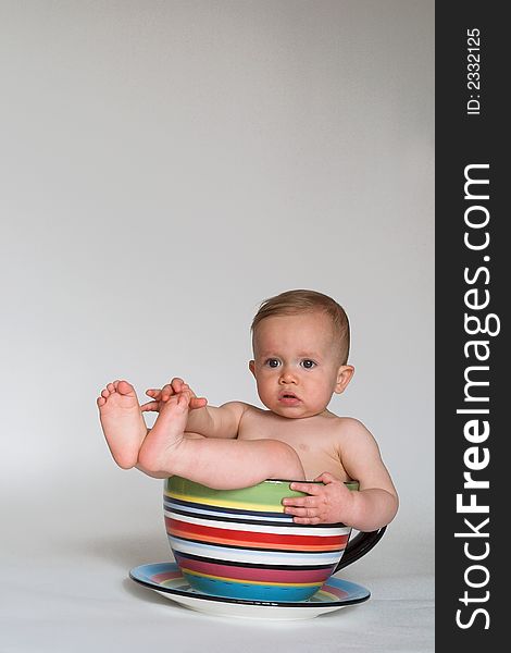 Image of an adorable baby sitting in a colorful, over-sized teacup. Image of an adorable baby sitting in a colorful, over-sized teacup