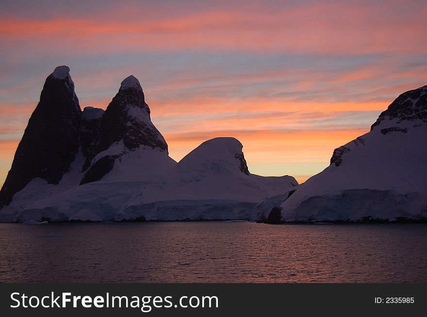 Beautiful sunrise colors with a partly ice covered rock formation in foreground in the ocean. Beautiful sunrise colors with a partly ice covered rock formation in foreground in the ocean