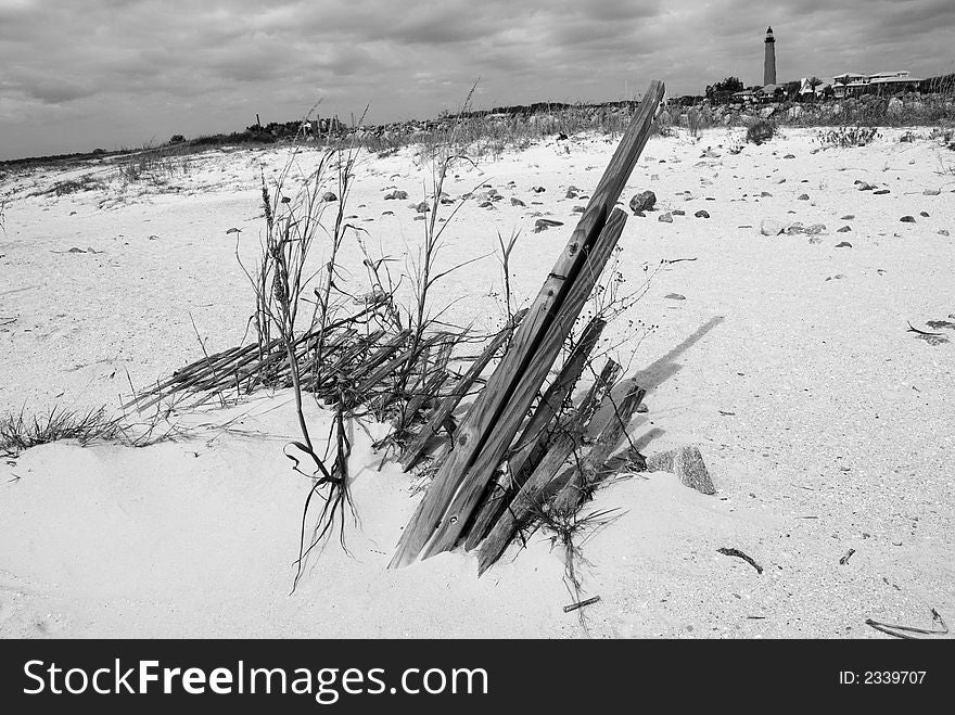 A dilapitated sand fence lies buries in the coastal dune sand with a lighthouse in the far distance. A dilapitated sand fence lies buries in the coastal dune sand with a lighthouse in the far distance