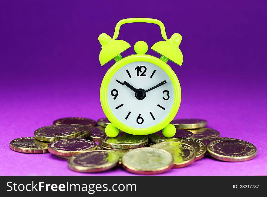 A lime green alarm clock placed on some golden coins, asking the question how long before your investment matures?. A lime green alarm clock placed on some golden coins, asking the question how long before your investment matures?
