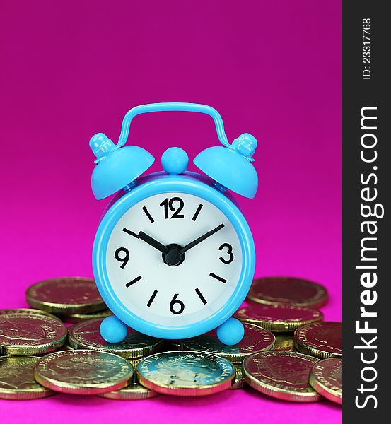 A light blue alarm clock placed on some golden coins with a purple background, asking the question how long before your investment matures?. A light blue alarm clock placed on some golden coins with a purple background, asking the question how long before your investment matures?