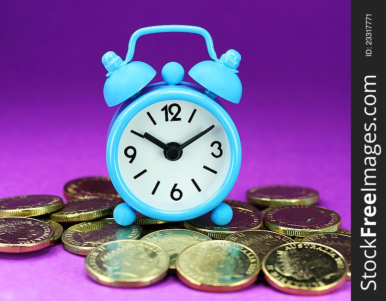 A light blue alarm clock placed on some golden coins with an orange background, asking the question how long before your investment matures?. A light blue alarm clock placed on some golden coins with an orange background, asking the question how long before your investment matures?