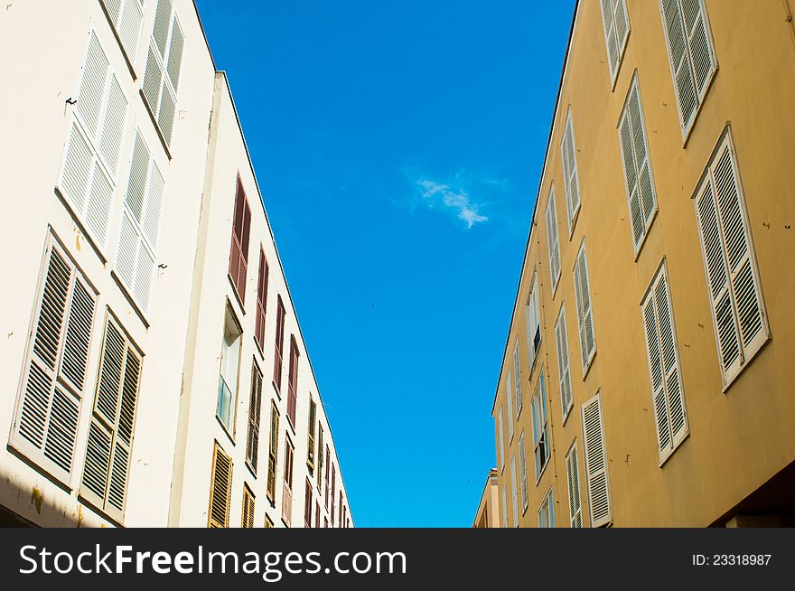 Two walls with closed windows opposite each other over blue sky