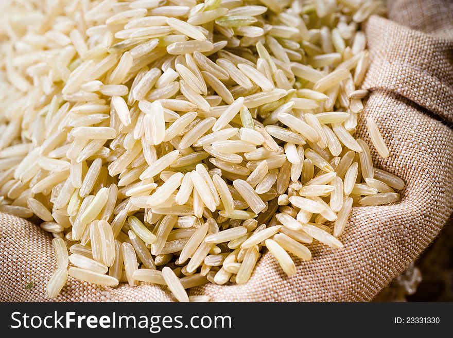 Raw long grain organic rice grain in burlap sack - selective focus