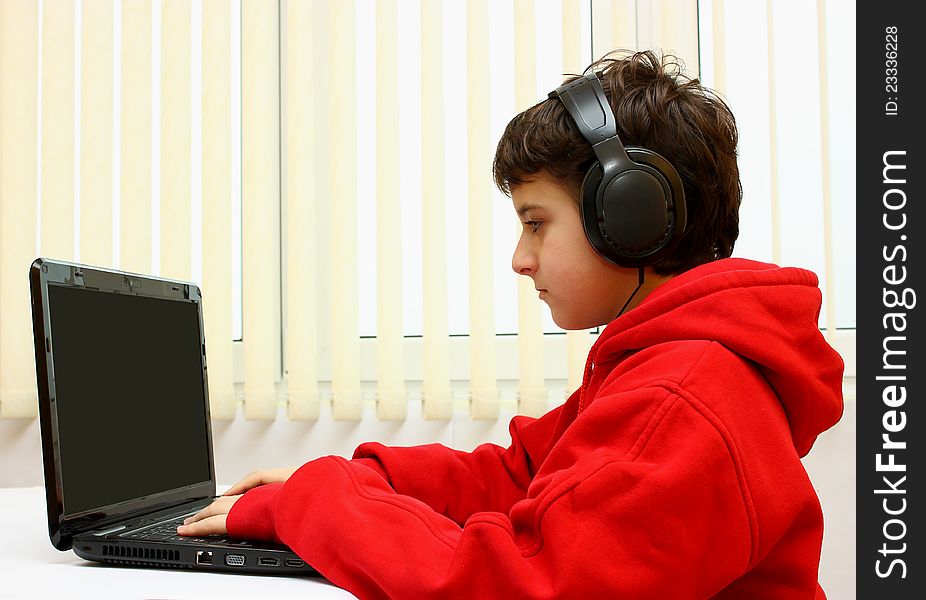 Boy working on a black laptop with headset at home (office). Boy working on a black laptop with headset at home (office)
