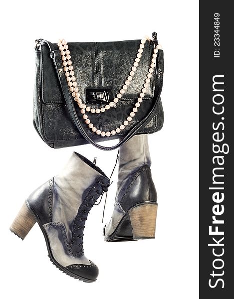 Pair of modern leather boots and woman silver purse with pearl necklace over white background. Pair of modern leather boots and woman silver purse with pearl necklace over white background