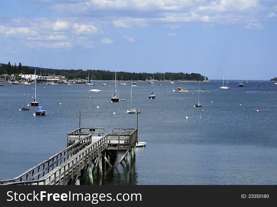 A wooden dock extends out into a harbor on the coast of southern Maine where boats lie at anchor. A wooden dock extends out into a harbor on the coast of southern Maine where boats lie at anchor