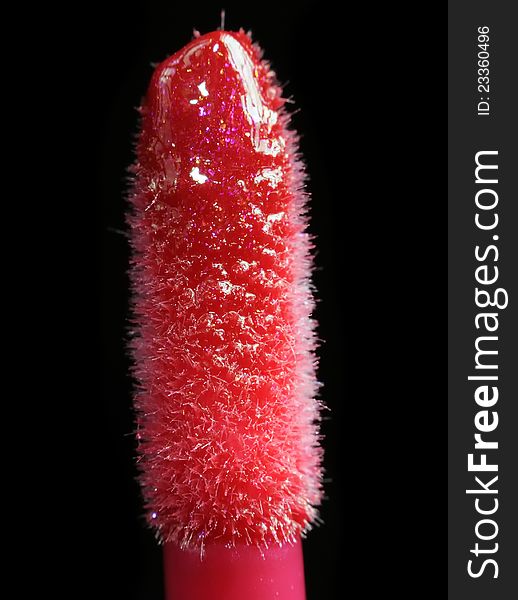 A close-up of a lip gloss applicator with red lip gloss on a black background. A close-up of a lip gloss applicator with red lip gloss on a black background