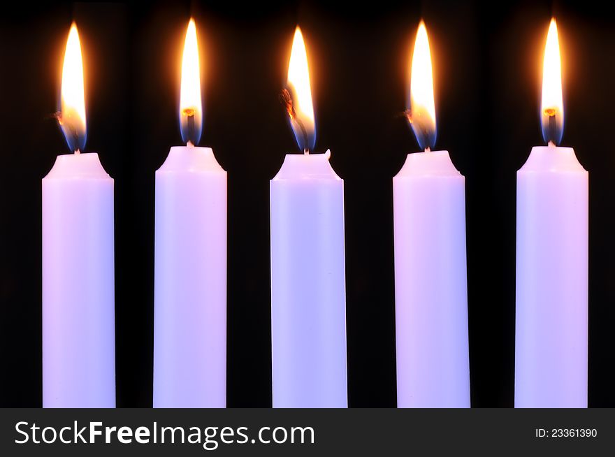 Five burning candles in a row on a black background. Five burning candles in a row on a black background