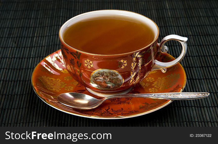 Porcelain teacup and saucer and a silver teaspoon on the bamboo pad, studio lights. Porcelain teacup and saucer and a silver teaspoon on the bamboo pad, studio lights