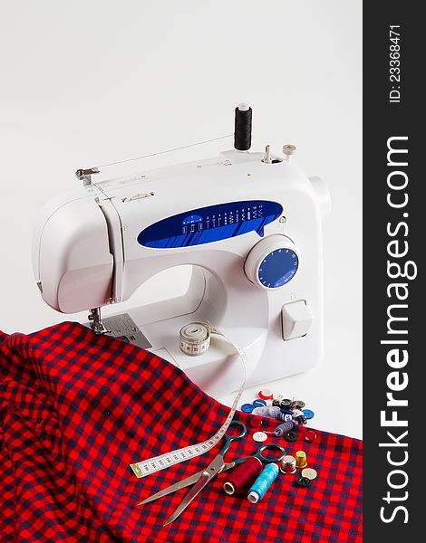 Sewing machine with red cloth, buttons, spool of thread, scissors, measuring tape