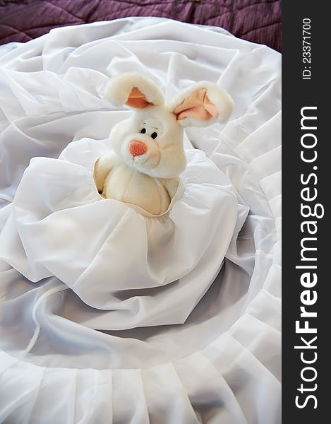Toy rabbit in wedding dress on bed