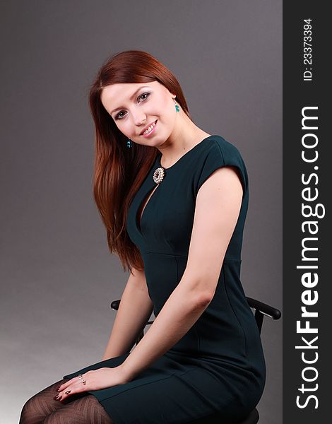 Adorable businesswoman in dark green dress sitting on a chair in a studio. Adorable businesswoman in dark green dress sitting on a chair in a studio