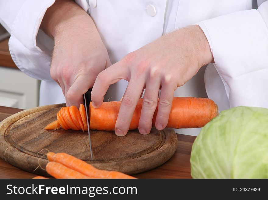 Chef preparing lunch and cutting carrot with knife