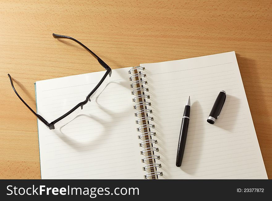 Notebook with pen and glasses on wooden table