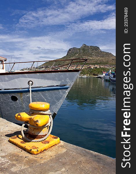 A boat moored in Houtbay Harbour, Cape Town with a mountain in the background and blue clouded skies. A boat moored in Houtbay Harbour, Cape Town with a mountain in the background and blue clouded skies