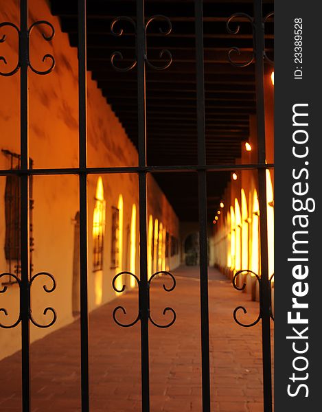 View of a long corridor at a mission with wrought iron window grates, brick floor and thick adobe walls all highlighted with evening sun. View of a long corridor at a mission with wrought iron window grates, brick floor and thick adobe walls all highlighted with evening sun