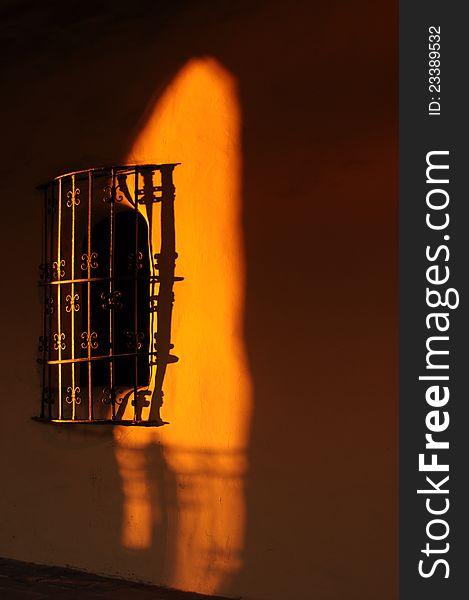 delicate wrought iron grate over a window in an adobe wall highlighted with setting sun golden light on the sdobe wall. delicate wrought iron grate over a window in an adobe wall highlighted with setting sun golden light on the sdobe wall