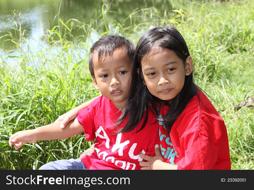 Little girl and her young brother were sitting at the edge of the lake.