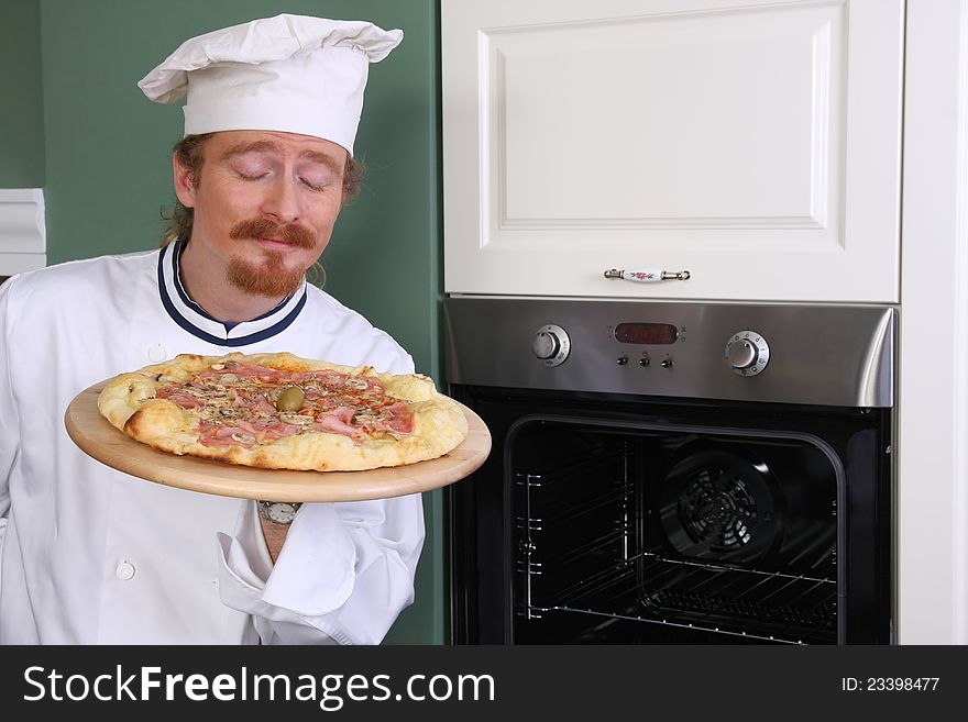 Young chef smelling italian pizza in kitchen