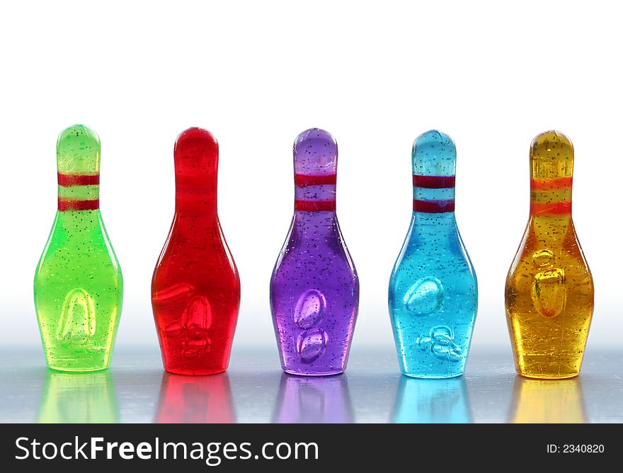 A row of colorful, miniature bowling pins with reflections, isolated on white. A row of colorful, miniature bowling pins with reflections, isolated on white.