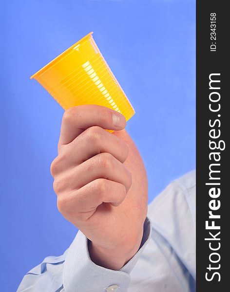 In man's hand bright, yellow, plastic glass on blue background. In man's hand bright, yellow, plastic glass on blue background