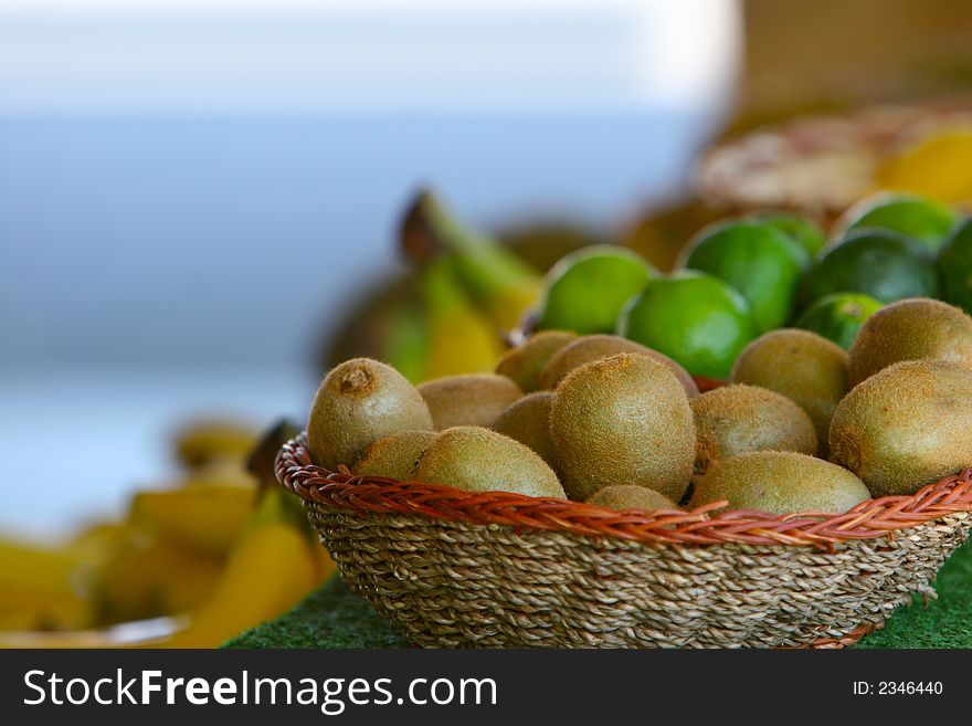 Kiwi in woven basket on green counter with assorted fruit in the background. Kiwi in woven basket on green counter with assorted fruit in the background