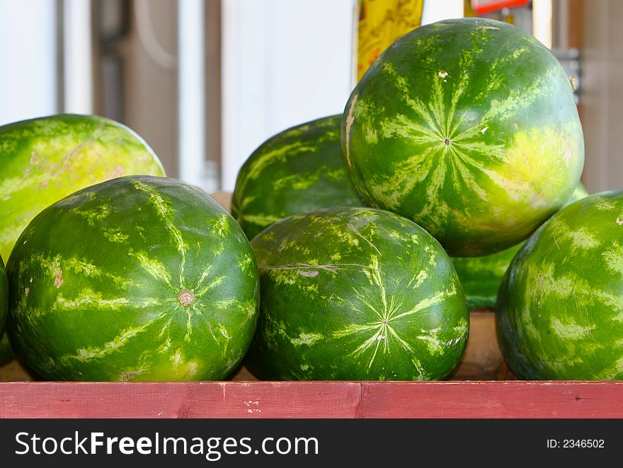 Large water melons on a red table under a shed outside